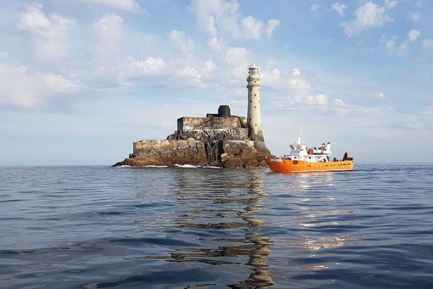 A lighthouse on a rocky outcrop with a boat in the foreground. 2