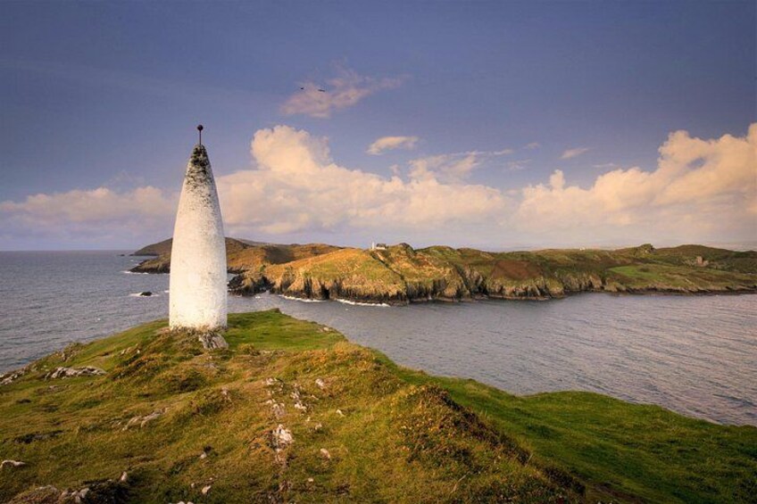 A coastal landscape with a white lighthouse on a grassy hill, a rocky shoreline, and a clear sky. 5