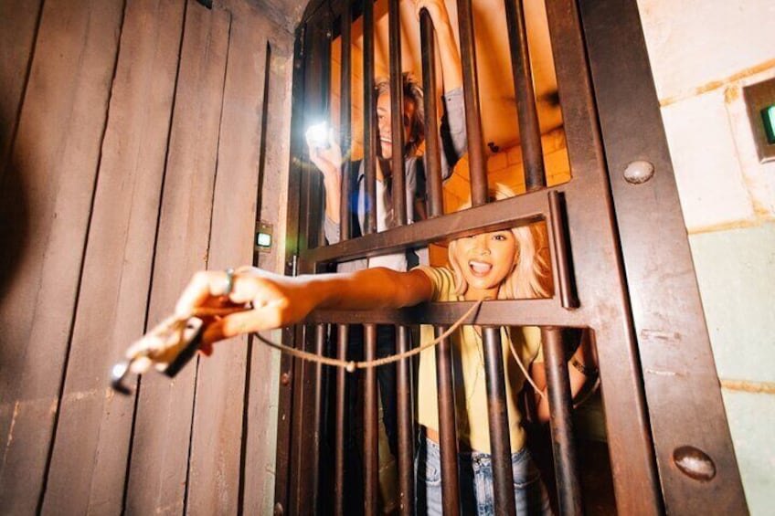 A hand holding a key near a wooden door with metal bars. 1