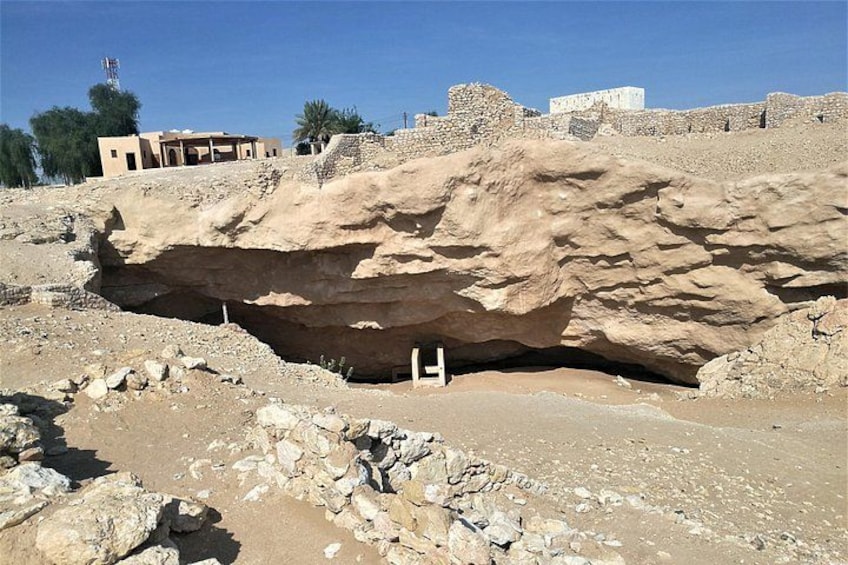 A rocky excavation site with a large cave-like structure, a small building, and a distant pyramid. 1