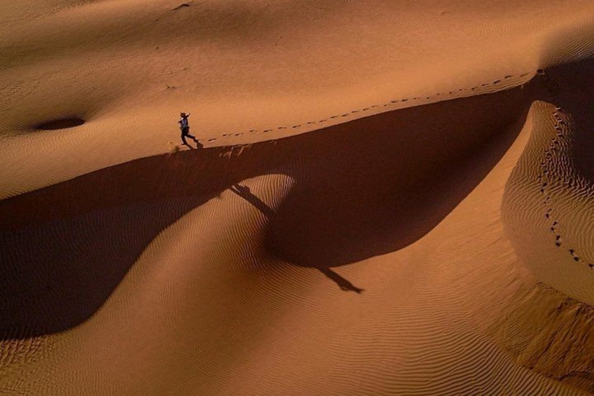 A person walking on a sand dune with ripples and a shadow. 2