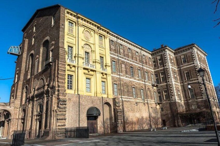 A historic building with yellow and brown brickwork, large windows, and a prominent clock tower. 4