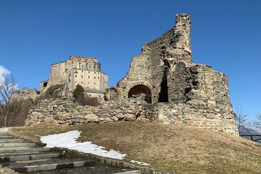 A historic stone structure with a large arched entrance, a smaller building in the background, and a snow-covered slope leading up to the ruins. 3