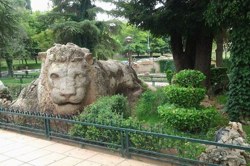 A large stone sculpture of a lion's head in a park with trees and a fence. 3