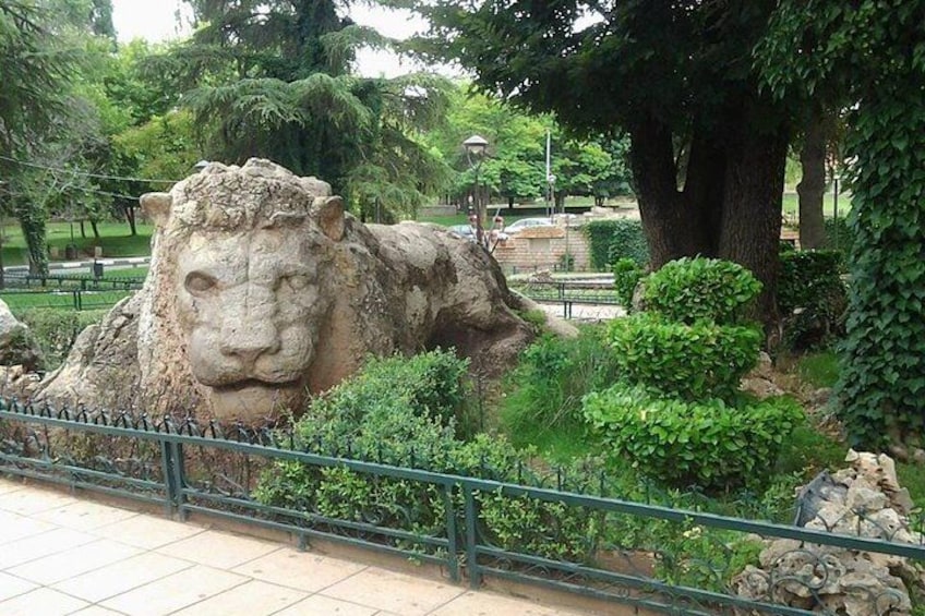 A large stone sculpture of a sheep's head in a park with trees and a fence. 3