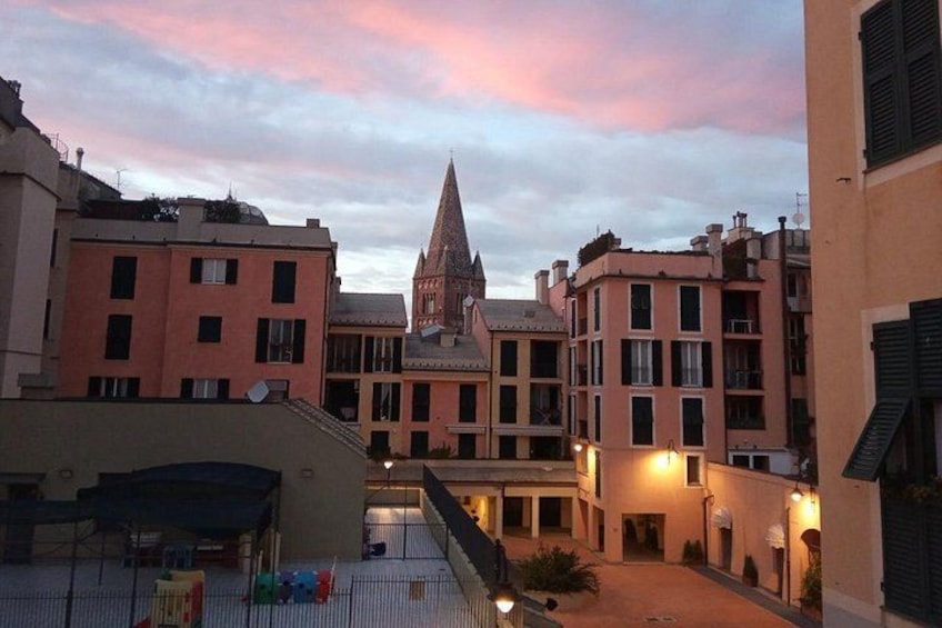 A courtyard with buildings, a church spire, and a sunset sky. 5