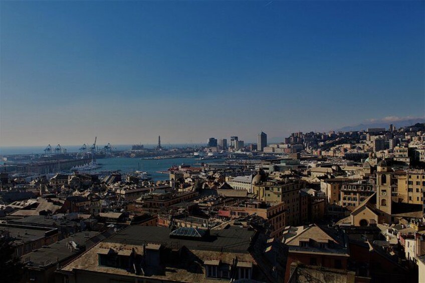 Un paisaje urbano costero con edificios densos, un puerto con barcos y grúas industriales. 3