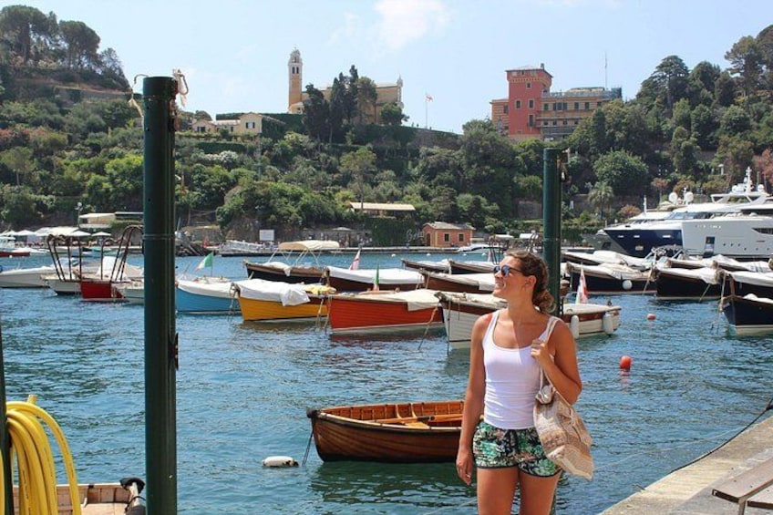 A marina with various boats docked, a person standing on the dock, and buildings in the background. 1