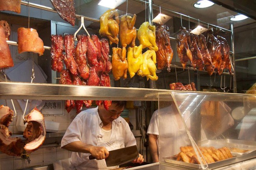 Un puesto de comida con diferentes carnes colgadas y un trabajador preparando alimentos. 1