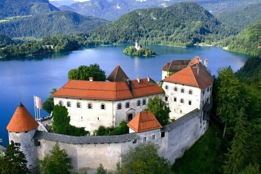 Ett slott med röda tak och en vallgrav, omgivet av frodig grönska och en sjö. 1