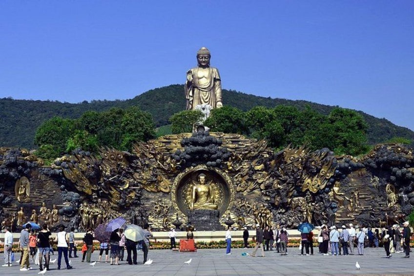 A large golden Buddha statue surrounded by intricate golden decorations, with people gathered around it. 1