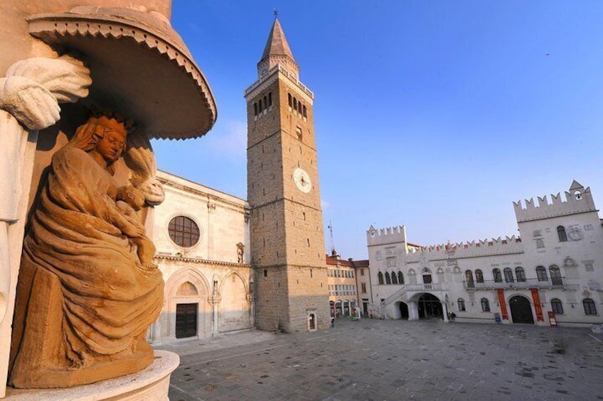 A historic square with a tall tower, a statue, and a castle-like building. 2