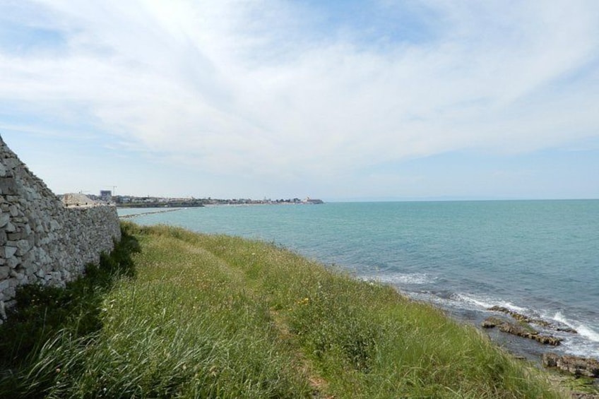 A coastal landscape with a stone wall, grassy path, and calm sea. 2