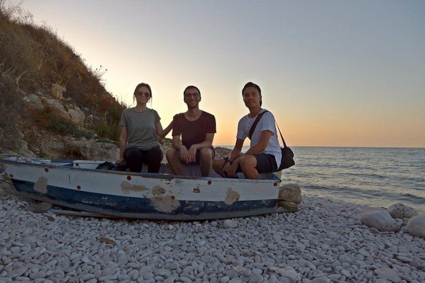 Three people sitting on a boat on a pebble beach with a sunset in the background. 5