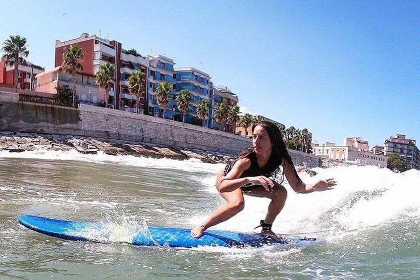 A person surfing on a blue board in the ocean with buildings and palm trees in the background. 4