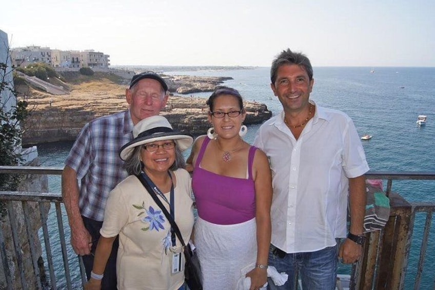A group of people standing on a balcony overlooking a coastal area with buildings and boats in the distance. 1