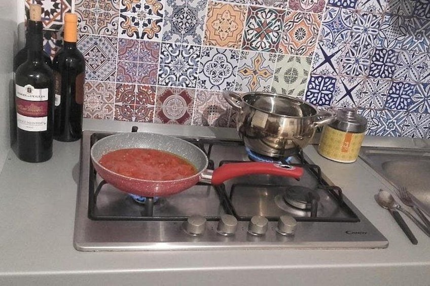 A kitchen with a gas stove, a red frying pan, a pot, and two bottles of wine. 3