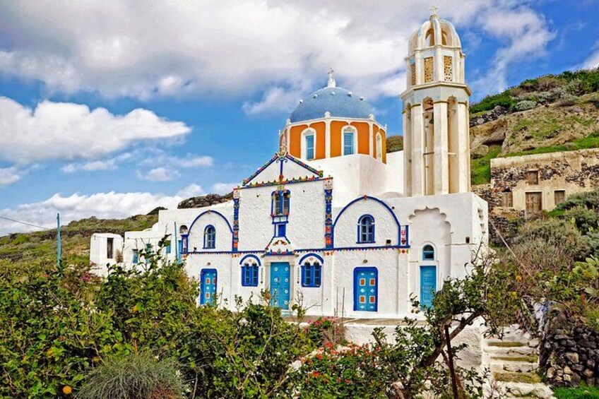 A white church with blue doors and a bell tower, surrounded by greenery and hills. 1