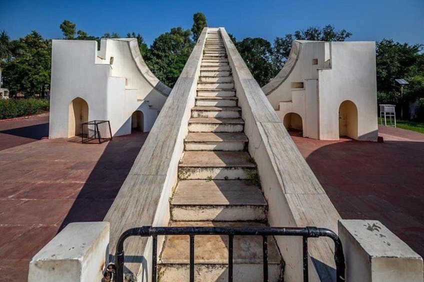 A concrete staircase leading up to a white structure with arched openings, surrounded by greenery. 3