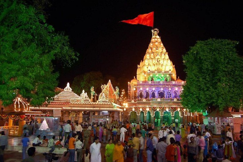 A temple with a red flag, illuminated by lights, and a crowd of people in front. 4