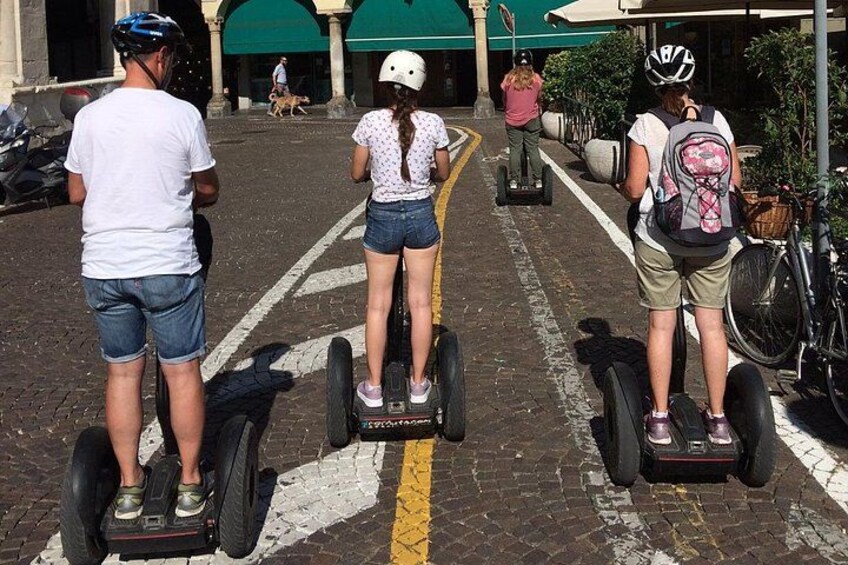 Tres personas en vehículos Segway en una calle adoquinada, con bicicletas estacionadas y un edificio al fondo. 2