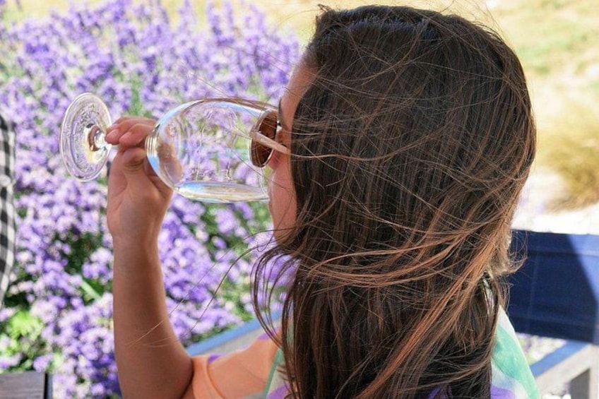 Una persona che tiene un bicchiere di vino, con fiori viola sullo sfondo. 3
