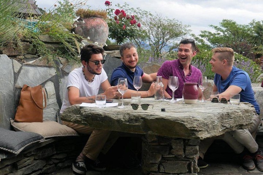 Quattro persone sedute a un tavolo di pietra all'aperto, con bevande e un vaso di fiori. 4