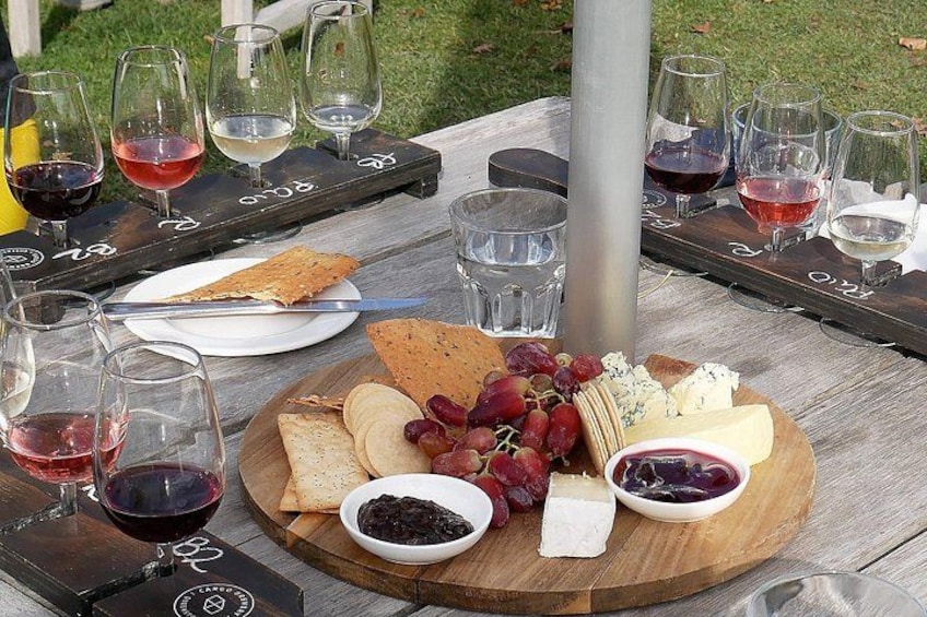 Un tavolo in legno con un tagliere di formaggi, grappe d'uva e bicchieri da vino. 2