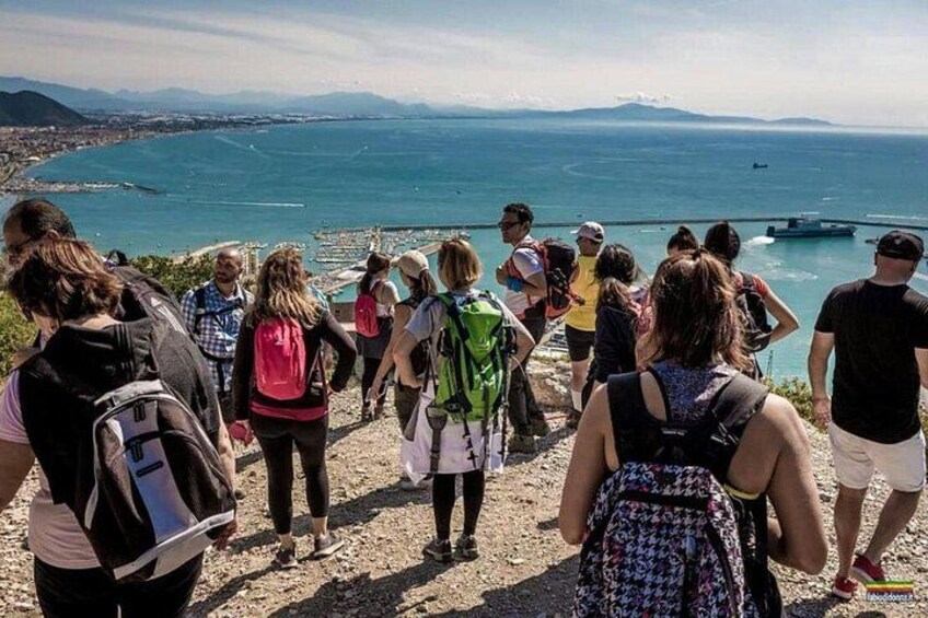 En gruppe vandrere på en stenet sti med udsigt over et kystområde og havet samt fjerne bjerge. 3