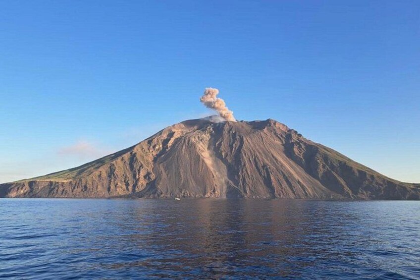 Una isla volcánica con una columna de humo elevándose desde su cima, rodeada de aguas tranquilas. 2