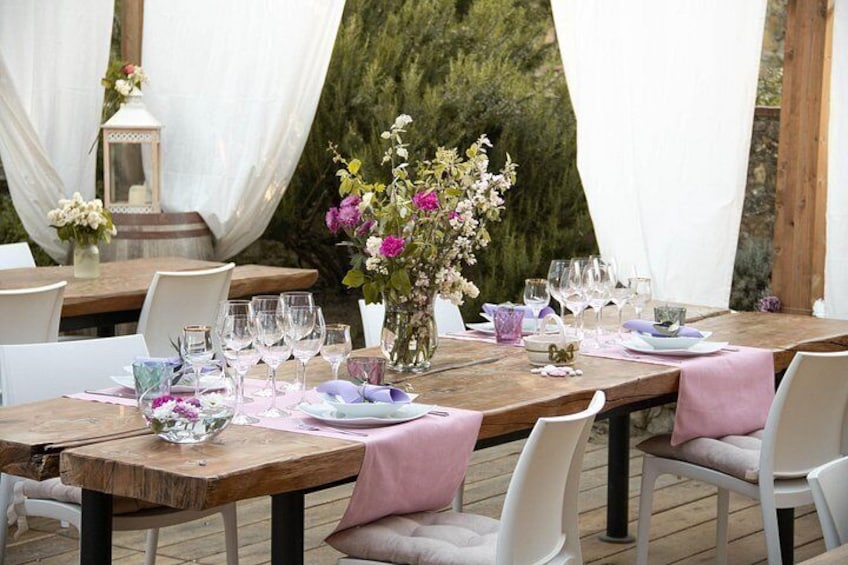 An outdoor dining setup with wooden tables, white chairs, pink tablecloths, and floral centerpieces. 4