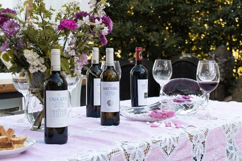 A table set outdoors with wine bottles, glasses, and a floral arrangement. 2