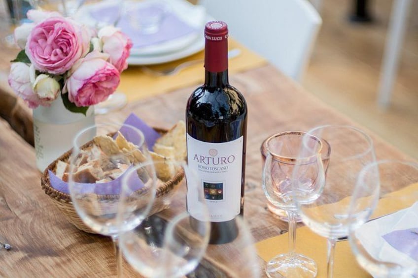 A bottle of Arturo wine, a basket of bread, and empty wine glasses on a wooden table. 4
