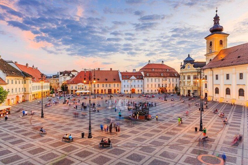 A square with buildings, a fountain, and people. 1
