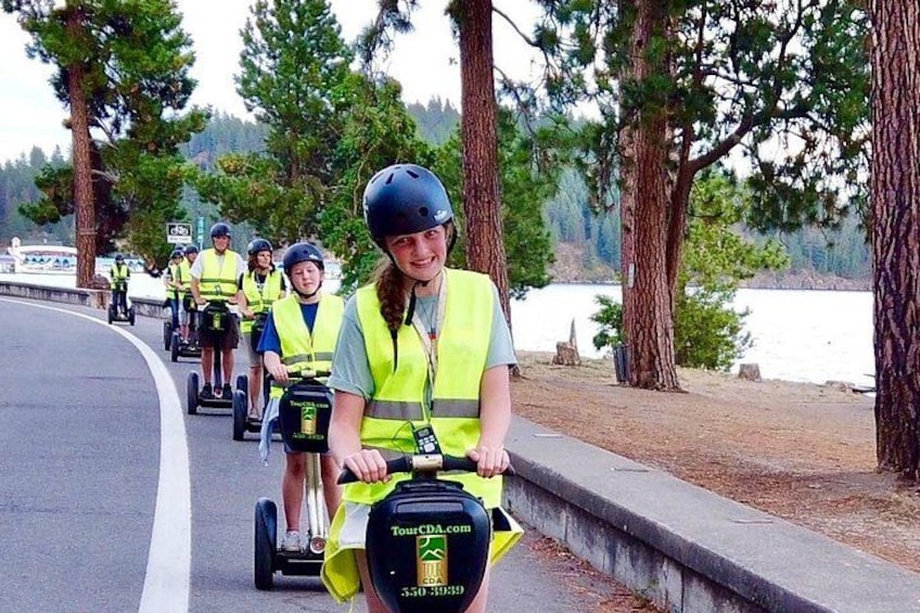 People riding Segways on a road with trees and a body of water in the background. 3