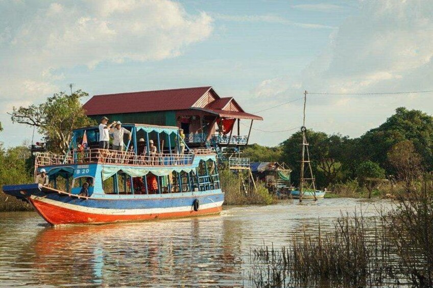 Een kleurrijke boot met passagiers, een steiger en een gebouw met een rood dak. 3