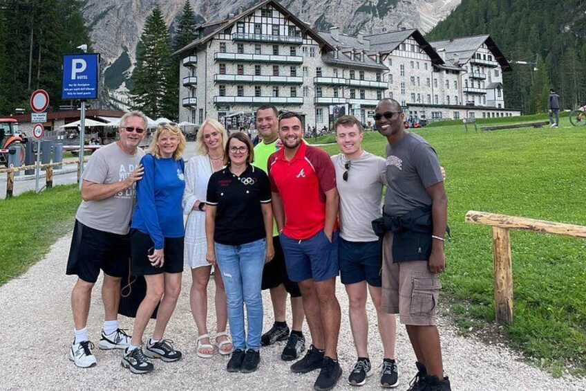A group of people posing in front of a mountain lodge with a parking sign and a wooden fence. 3
