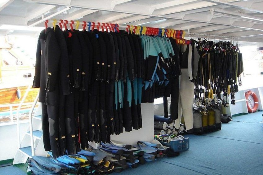 Diverse duikuitrusting, waaronder wetsuits en duikmaskers, uitgestald op een schepsdek. 2