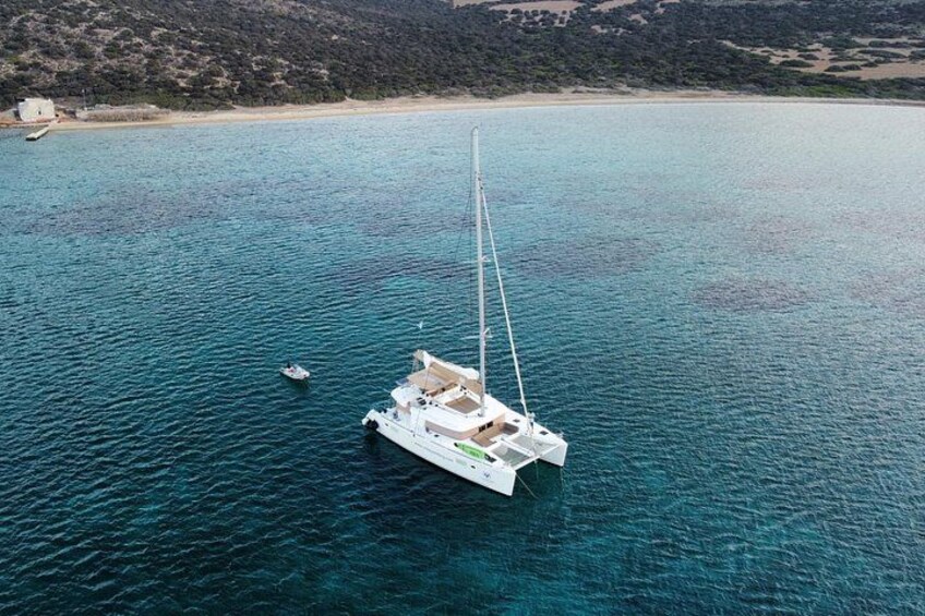 A sailboat anchored in a turquoise sea with a sandy beach and rocky hills in the background. 5
