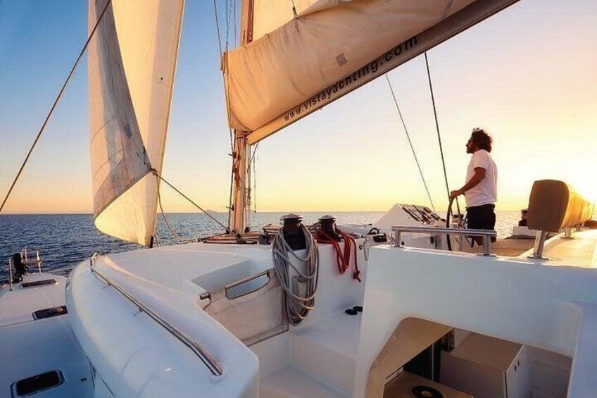 Eine Segelyacht mit einer Person am Steuer, einem wolkenlosen Himmel und ruhigem Wasser. 3