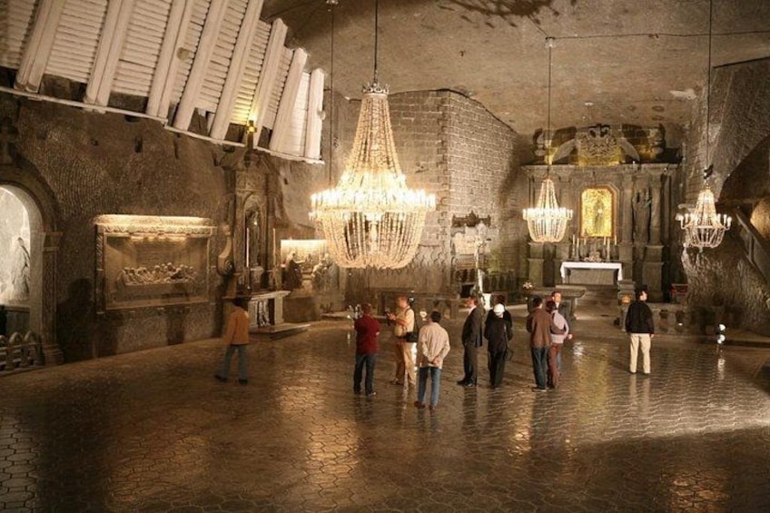 An indoor historical site with stone walls, chandeliers, and visitors. 2