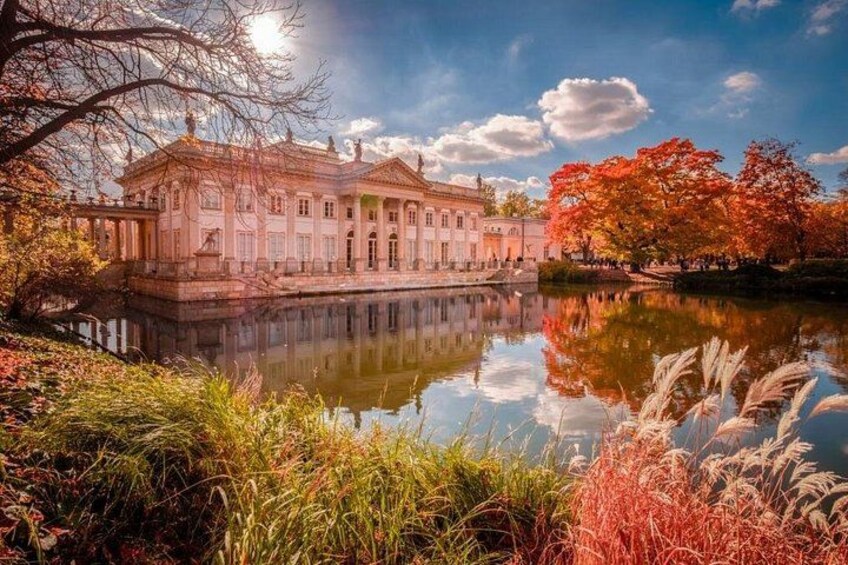 A classical building with a reflective water body in front, surrounded by autumn foliage. 2
