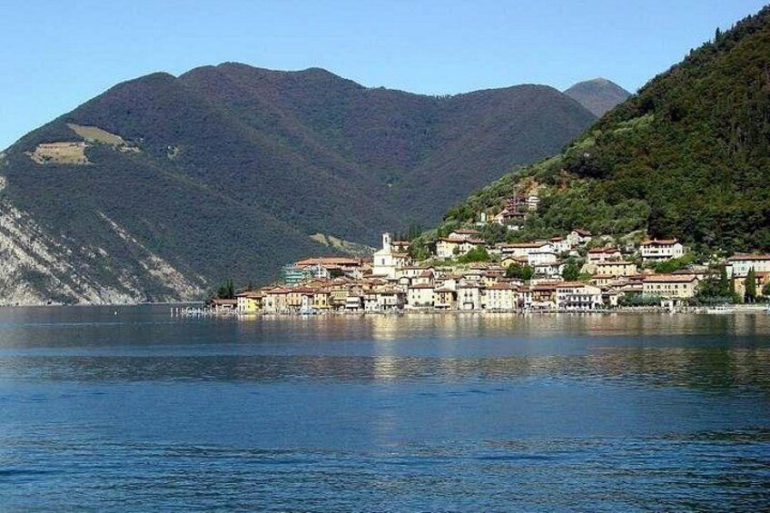 A coastal town with buildings along the water, mountains in the background, and calm water. 3
