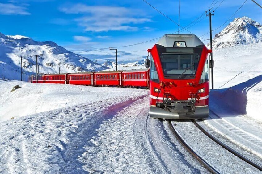 A red train on tracks in a snowy mountainous area. 1