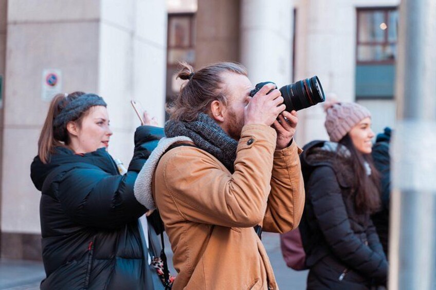Une personne prend une photo avec un appareil photo, une autre personne tient un téléphone et une troisième personne se trouve à l’arrière-plan. 3