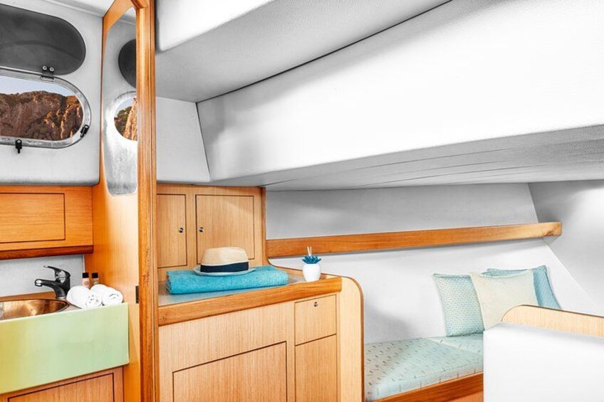 Una cabina compatta e ben organizzata, con mobili in legno, un piccolo lavandino e un'accogliente area salotto con cuscini. 5