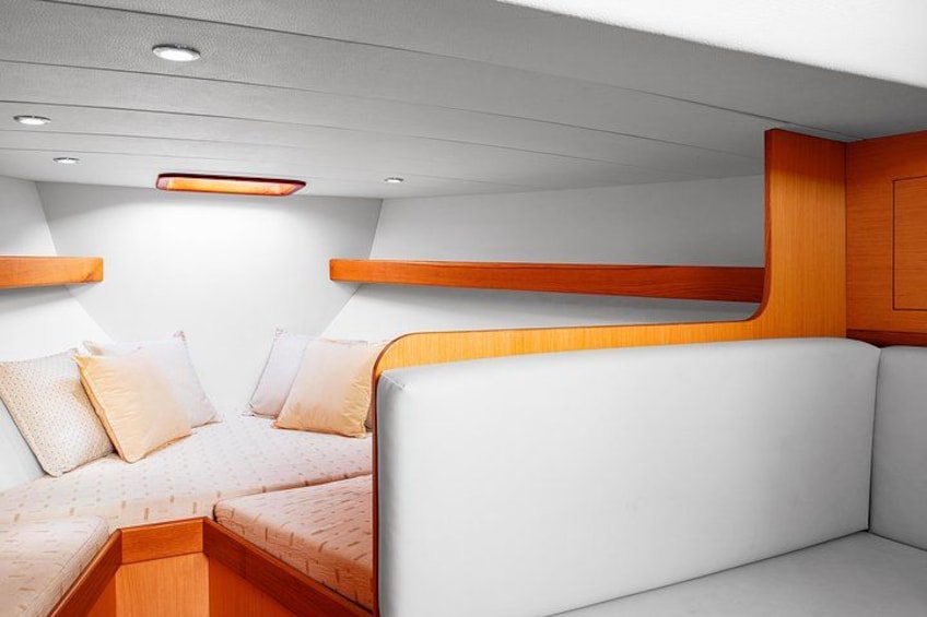 Interno di una barca con una panca imbottita bianca, elementi in legno e una piccola luce a soffitto. 3