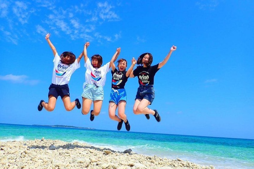 Four people jumping on a beach with clear blue sky and ocean in the background. 3