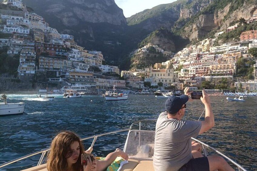 A boat on water with a person taking a photo, a woman looking at a device, and a coastal town with buildings. 3