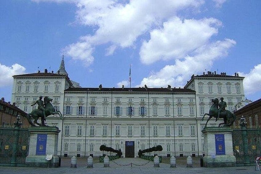 Un gran edificio de estilo clásico con estatuas de jinetes a caballo, una entrada central destacada y un cielo azul despejado. 2